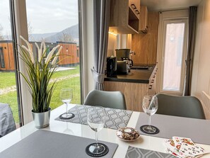 Een eetgedeelte met een tafel gedekt voor twee personen, een potplant en uitzicht op de keuken en buitenruimte.
