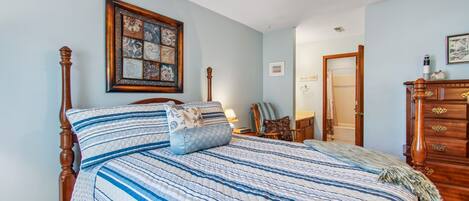 A bedroom with a large bed, a ceiling fan, a wooden dresser, and a framed artwork on the wall.