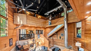A spacious log cabin interior with a central living area, a staircase, and a bar area. - The Roundhouse Lodge | Pet-Friendly Game Retreat (Broken Bow)