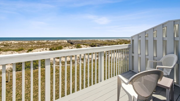 A balcony with white railings and two white chairs, overlooking a beach with dunes and a pier. - Amelia Island 2BR Renovated Townhome near the Ritz Carlton - Sandpiper VIlla (Fernandina Beach)