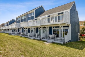 A row of beach houses with balconies, outdoor seating, and a grassy lawn.
