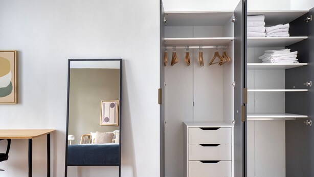 A bedroom with a bed, a bedside table, a mirror, and a wardrobe with shelves and hanging space.