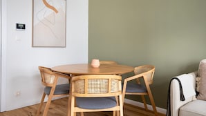 A dining area with a round wooden table and four chairs, a framed abstract artwork on the wall, and a thermostat on the wall.