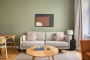 Ein Wohnzimmer mit einer Couch, einem runden Holztisch, einem Beistelltisch mit Lampe und einem gerahmten abstrakten Gemälde an der Wand.