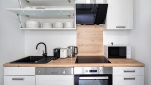 A modern kitchen with white cabinets, a wooden countertop, a black sink, a kettle, a toaster, a microwave, and a dishwasher.