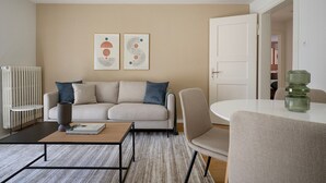 Un salon moderne avec un canapé, une table basse et un coin repas avec des chaises. Deux œuvres d’art encadrées ornent le mur.
