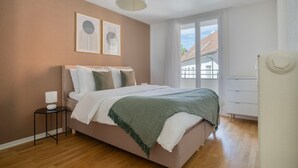 Une chambre à coucher avec un lit, une table de chevet et une fenêtre donnant sur des immeubles.