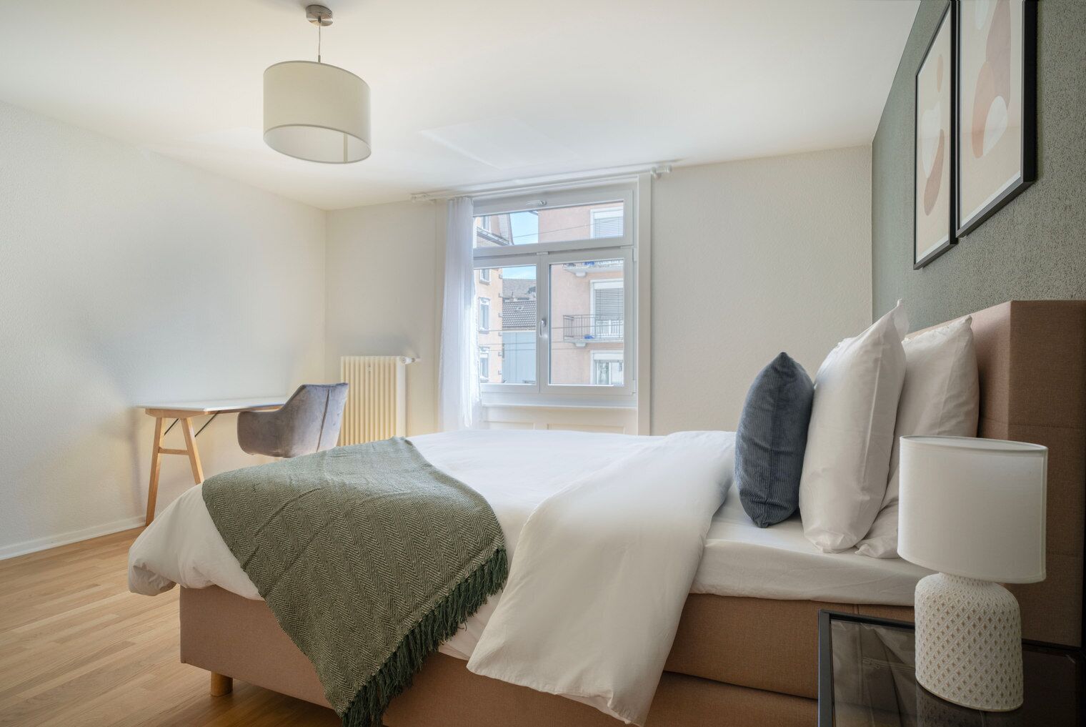 Una habitación de hotel moderna con una cama grande, un escritorio y una ventana con vistas a edificios.