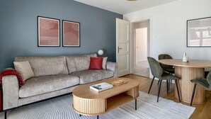 Un salon moderne avec un canapé gris, une table basse en bois et un coin repas comprenant une table ronde et des chaises.