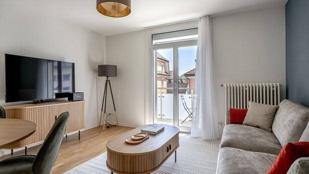 Un salon moderne avec un téléviseur à écran plat, une table à manger en bois, un canapé et une lampe sur pied.