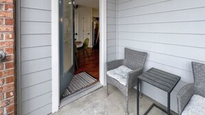 A porch with two grey upholstered chairs and a small table, a door leading to an interior space, and a brick wall on one side. - BLUES LANDING
The best stay between Main and the Mississippi!! (Memphis)