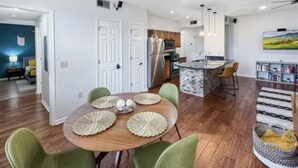 A modern kitchen with wooden cabinets, a central island, and a dining area with a round table and green chairs. - BLUES LANDING
The best stay between Main and the Mississippi!! (Memphis)