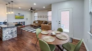 A modern kitchen with a central island, a dining area with a round table and green chairs, and a living room with a sofa and a television. - BLUES LANDING
The best stay between Main and the Mississippi!! (Memphis)