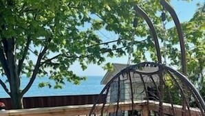 Eine Holzdielen-Terrasse mit einer Hängematte, einer rot-weiß karierten Tischdecke und Blick auf das Meer.