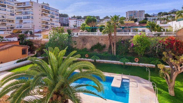 A pool area with palm trees, a white fence, and a view of surrounding buildings.