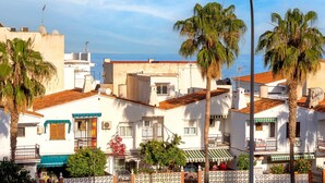 A coastal town with white buildings, palm trees, and a clear blue sky.