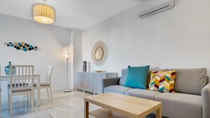 A modern living room with a grey sofa, a wooden coffee table, and a dining area with a white table and chairs.