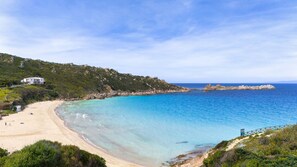 Un paysage côtier avec une plage de sable, des eaux bleues et limpides, et un promontoire rocheux.