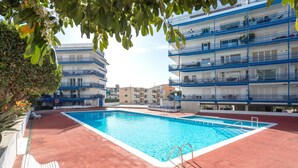 Piscina com deck vermelho, rodeada por edifícios altos com varandas.