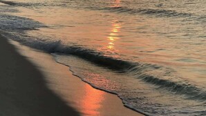 Een strand met een zonsondergang boven de oceaan, golven spoelen zachtjes aan op het strand.