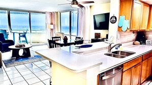 Een moderne keuken met een centraal eiland, een zithoek met stoelen en uitzicht op de oceaan door grote ramen.