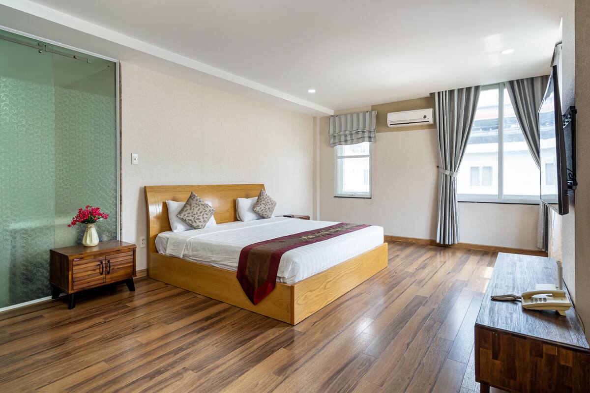 A bedroom with a wooden bed, a nightstand, a desk, and a window with curtains.