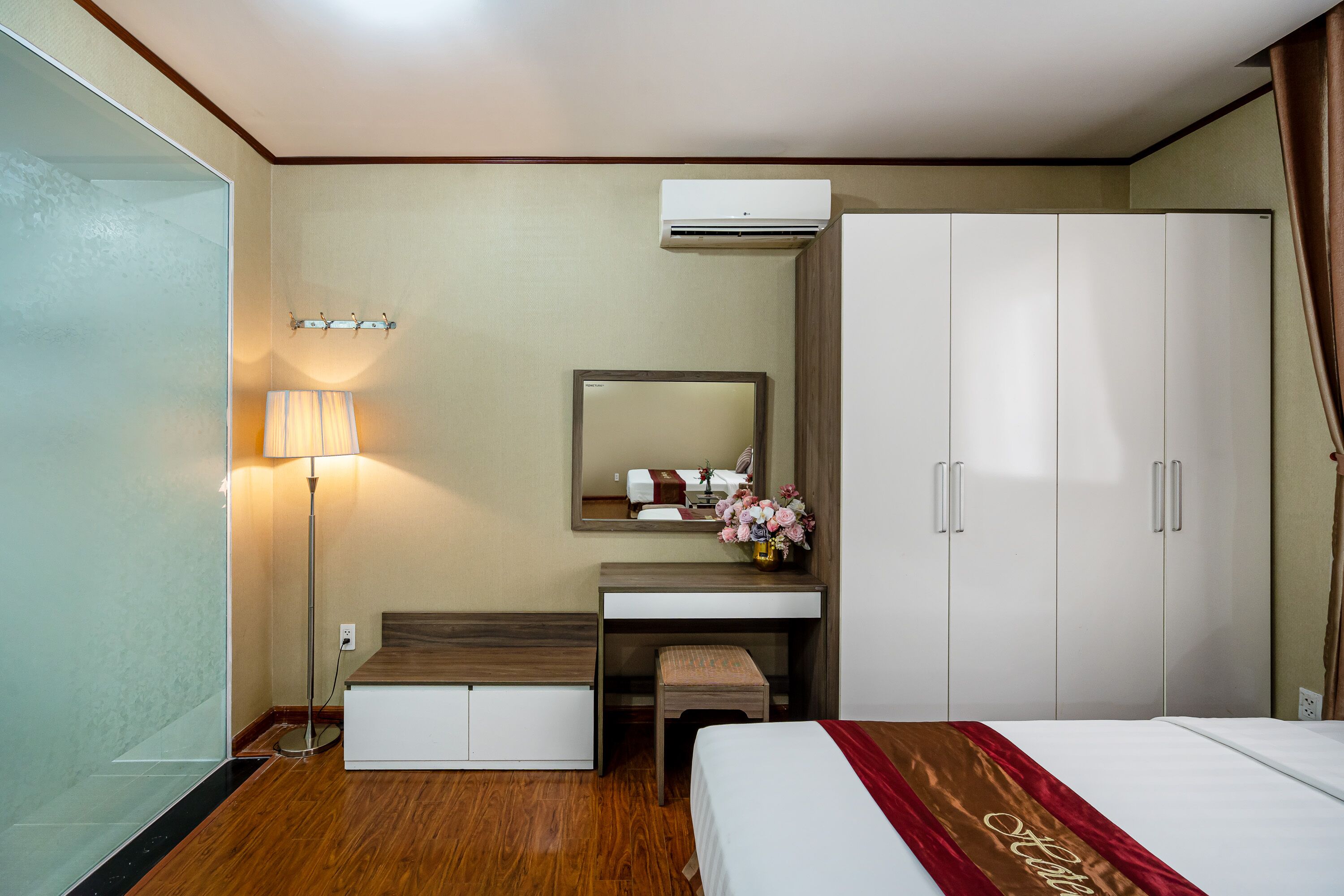 Quarto de hotel com cama, escrivaninha, espelho, guarda-roupa e unidade de ar condicionado.