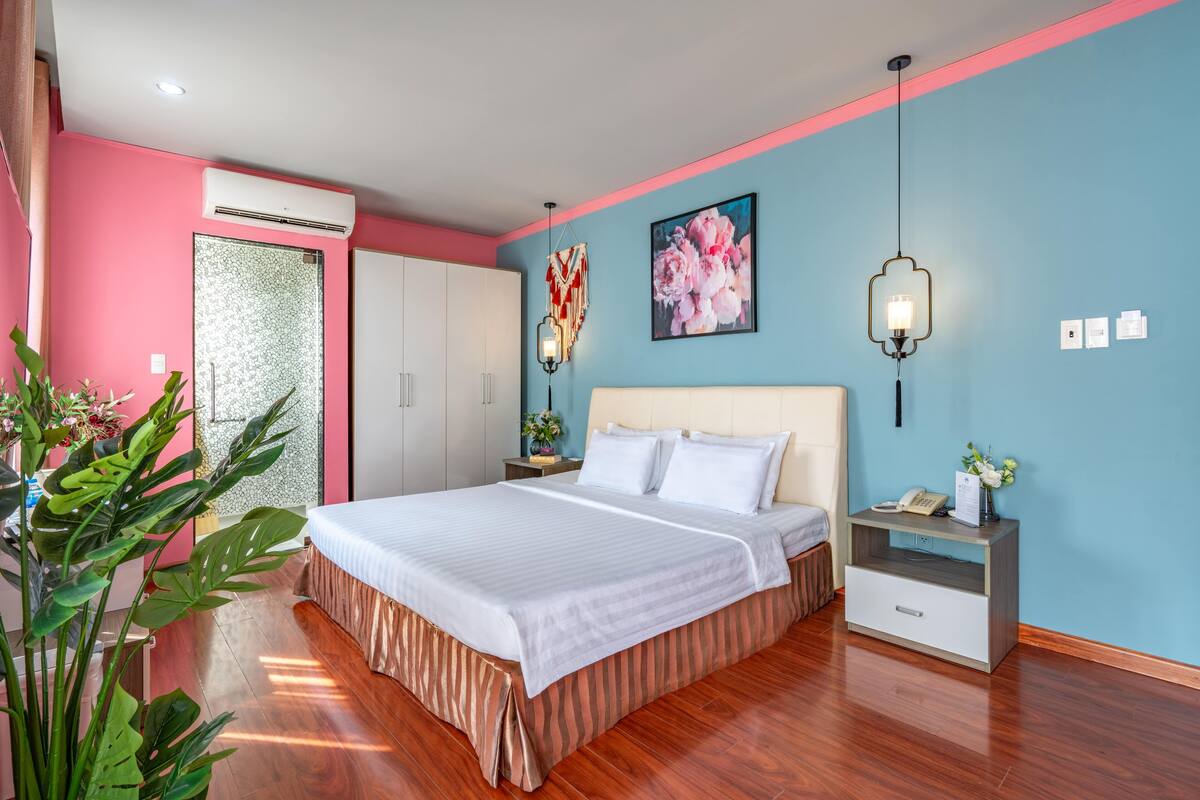 A bedroom with a bed, bedside tables, a nightstand, a wall-mounted lamp, and a large window.