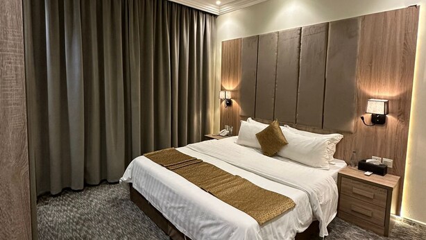 Habitación de hotel con una cama grande, cabecera de madera, dos mesitas de noche con lámparas y suelo cubierto de alfombra.