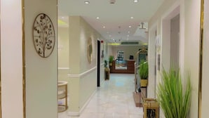 Un pasillo de hotel con mostrador de recepción, una planta y un elemento decorativo en la pared.