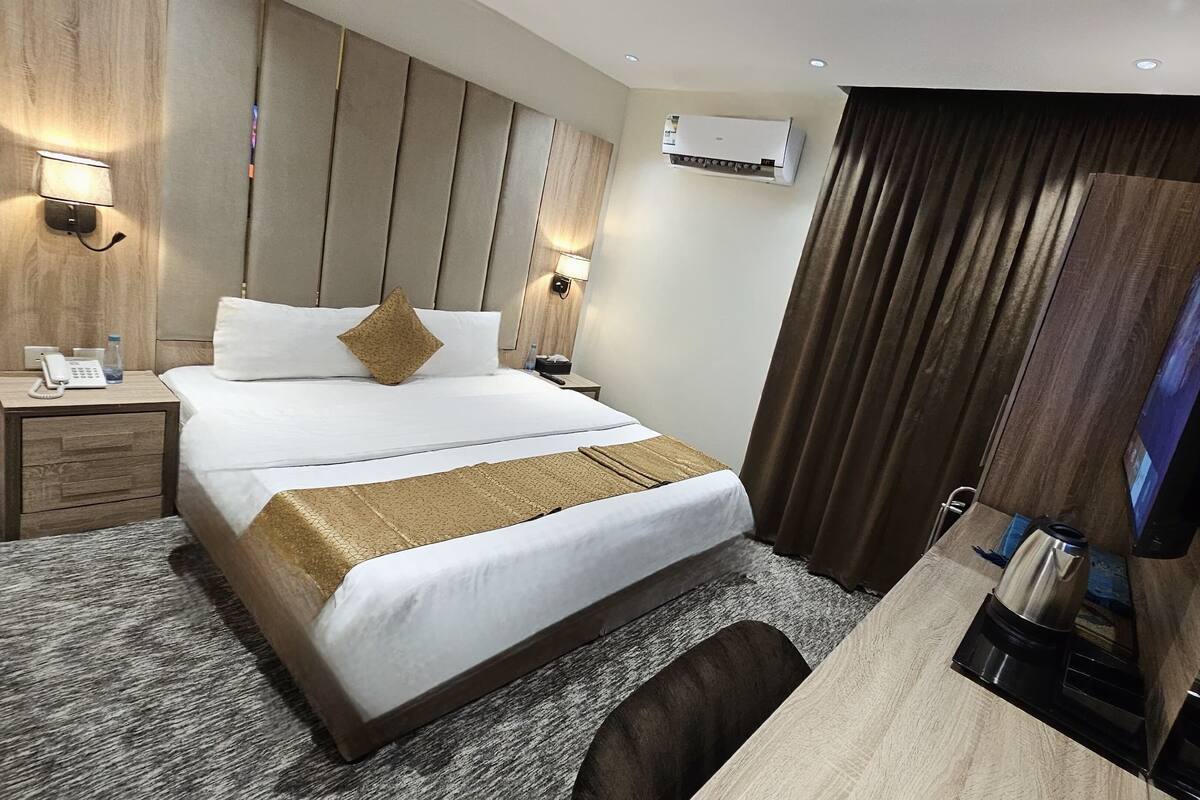 Une chambre d’hôtel avec un grand lit, des tables de chevet, un bureau avec une bouilloire et un appareil de climatisation.