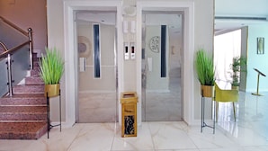 Un vestíbulo de hotel con suelo de mármol, una escalera y dos plantas en macetas.