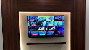 Un salón moderno con un televisor de pantalla plana montado en una pared de madera, un control remoto en el suelo y una caja de pañuelos sobre una mesita auxiliar.