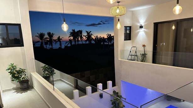 Una sala de estar moderna con un televisor de pantalla plana grande, lámparas colgantes y una barandilla de cristal con vistas a una piscina.