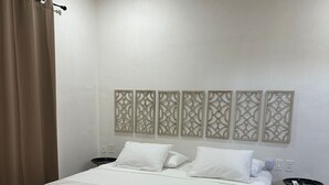 Un dormitorio ordenado con una cama grande, una mesita de noche, una lámpara de pared y un panel decorativo.