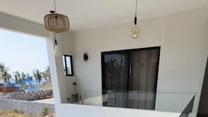 Un interior moderno con balcón de vidrio que da a una piscina y vistas a palmeras.