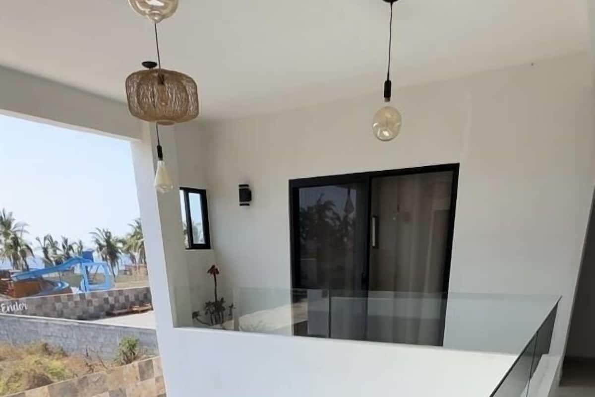 Een modern interieur met een glazen balkon met uitzicht op een zwembad en palmbomen.