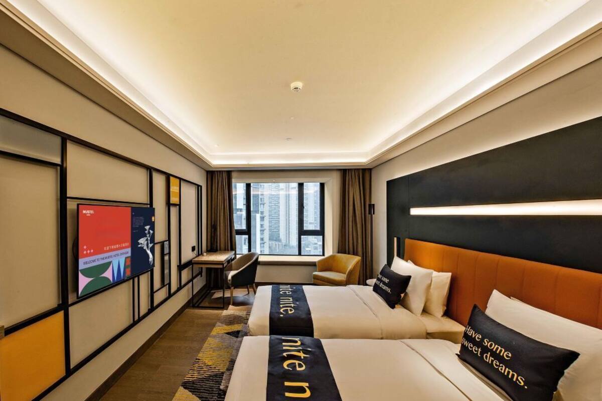 Habitación de hotel moderna con dos camas, un escritorio y un amplio ventanal con vistas a la ciudad.