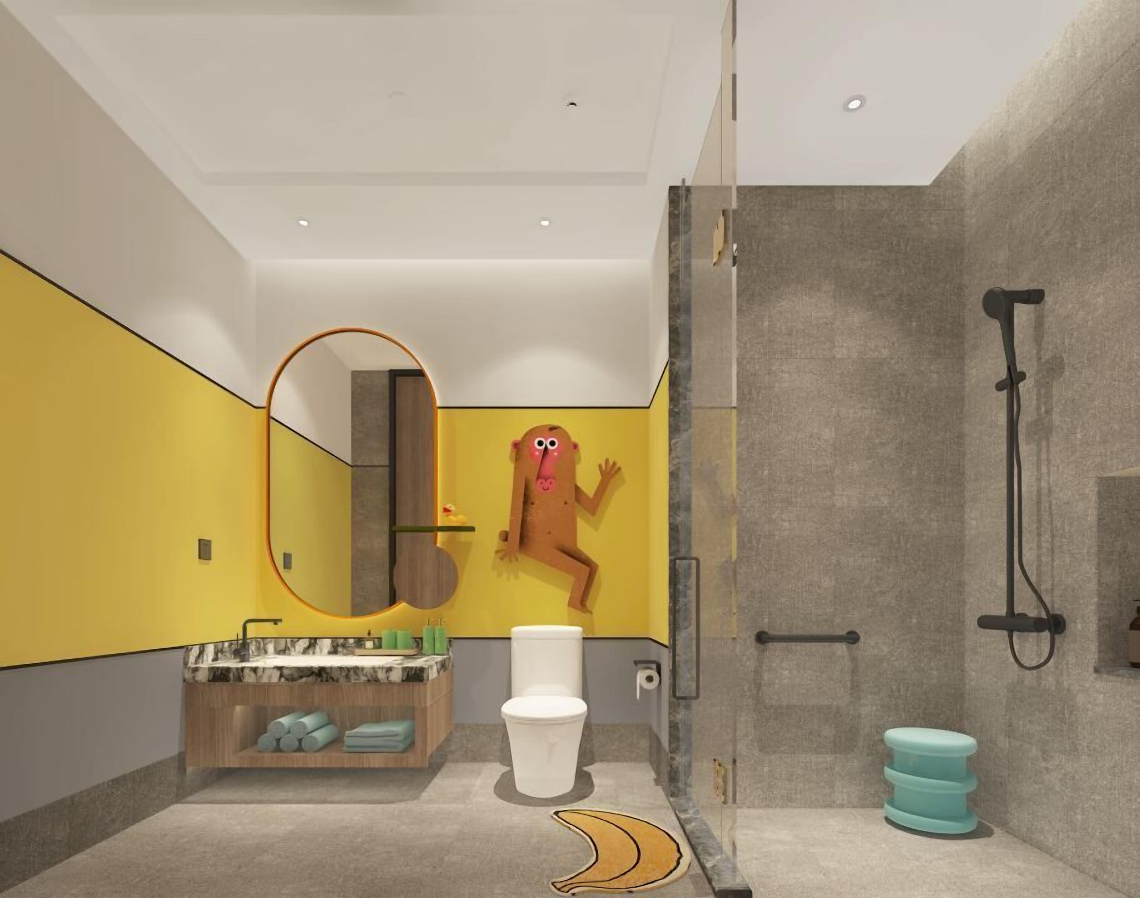 Un baño moderno con una pared de acento amarilla, un espejo grande, un inodoro, zona de ducha y una decoración con un personaje de dibujos animados único.