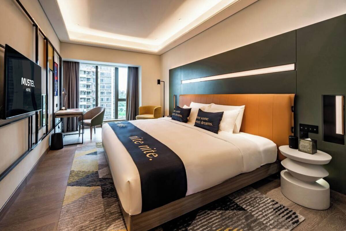 Habitación de hotel con una cama grande, un escritorio, una silla, un televisor y vistas de la ciudad.