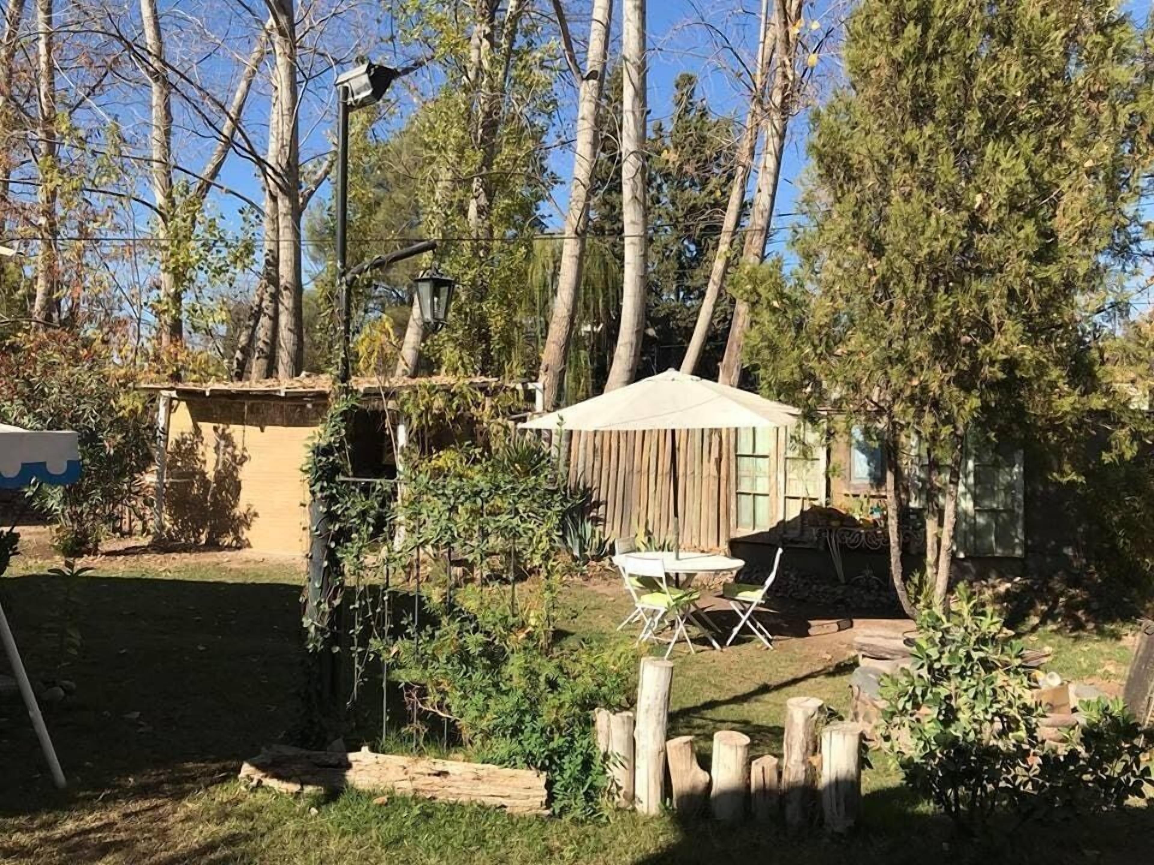 A rustic outdoor area with a wooden structure, a small table with chairs, and a hanging light fixture.