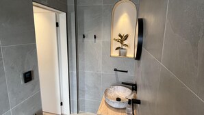 A modern bathroom with a round basin, a wall-mounted mirror, and a toilet paper holder.