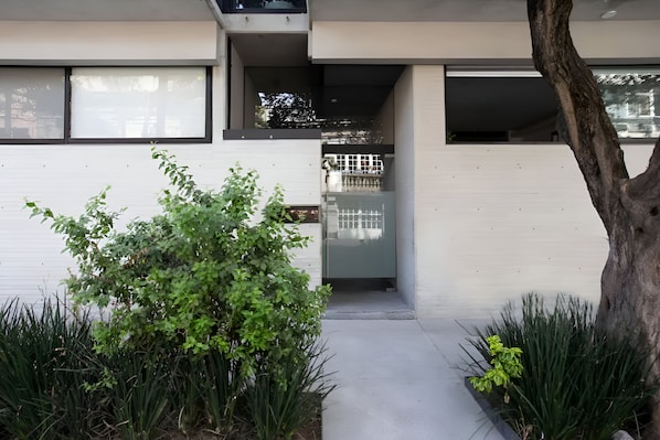 Stylish entrance with a glass door leading to a covered outdoor area surrounded by lush greenery.