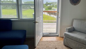 A room with a blue sofa, a striped armchair, and a door leading to a balcony with a view of a green landscape and a body of water.