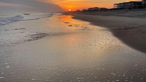 A beach with a sunset, waves, and buildings in the background.