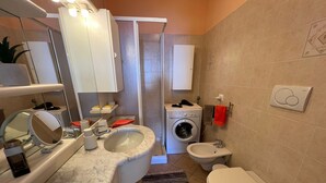 Et lille badeværelse med vask, spejl, toilet og vaskemaskine.