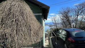 Et hus med en stor væg af stråballer, en bil foran og udsigt til bjerge og en sø.