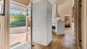 Un intérieur moderne avec une grande ouverture qui donne sur un patio, une cuisine dotée d’un four encastré et un escalier apparent.