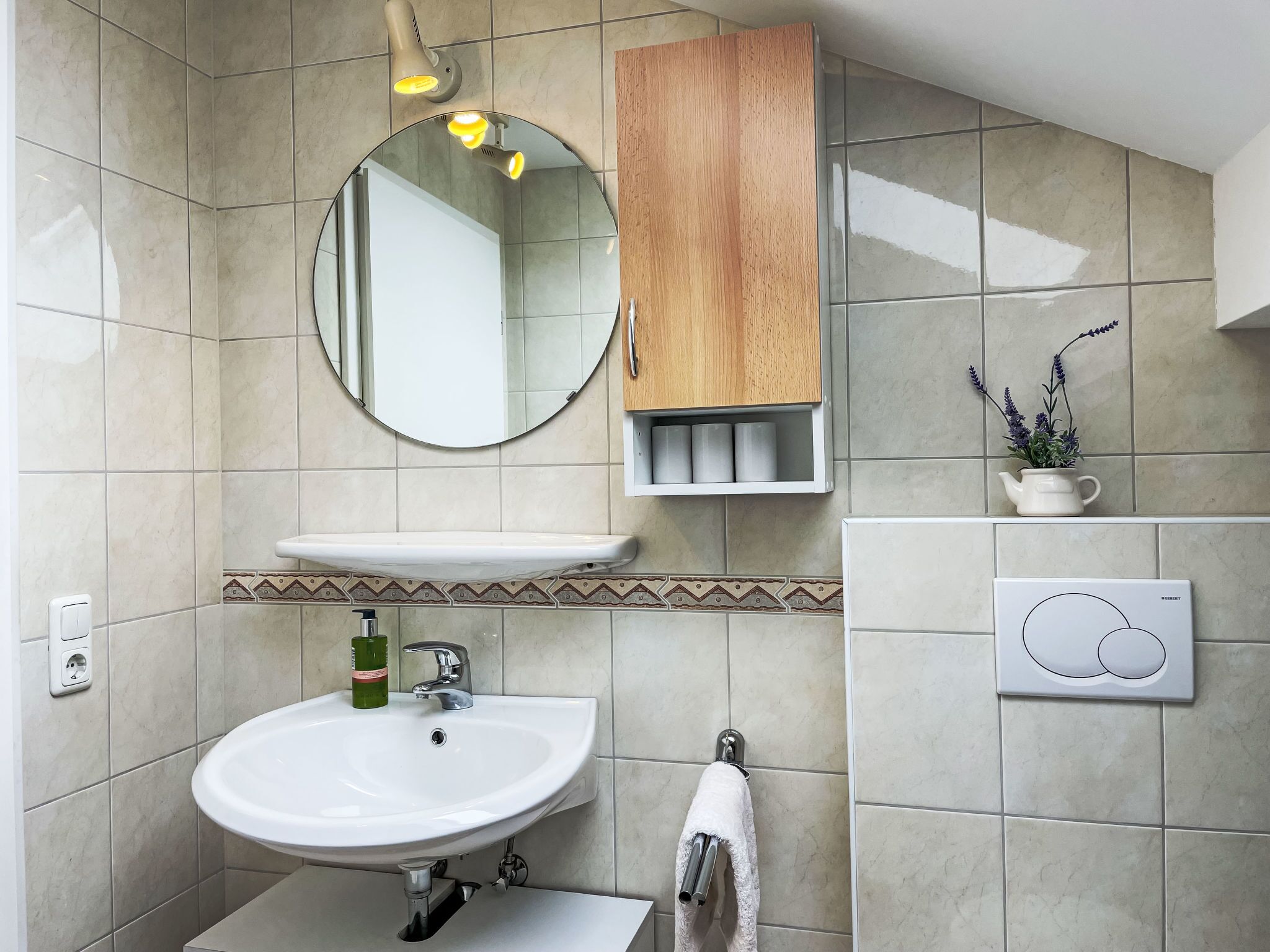 A bathroom with a round mirror, a wooden cabinet, a sink, and a towel rack.