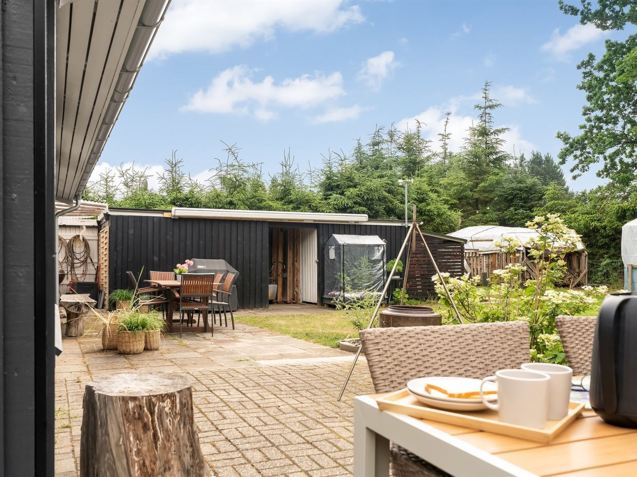 A patio with a table and chairs, a grill, and a covered outdoor area with a shed in the background.